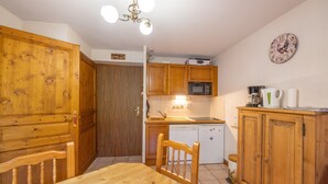 A kitchen with wooden cabinets, a microwave, a sink, and a dining table with chairs. - Apartment 'Le Jardin Des Neiges' with Balcony (Praz-sur-Arly)
