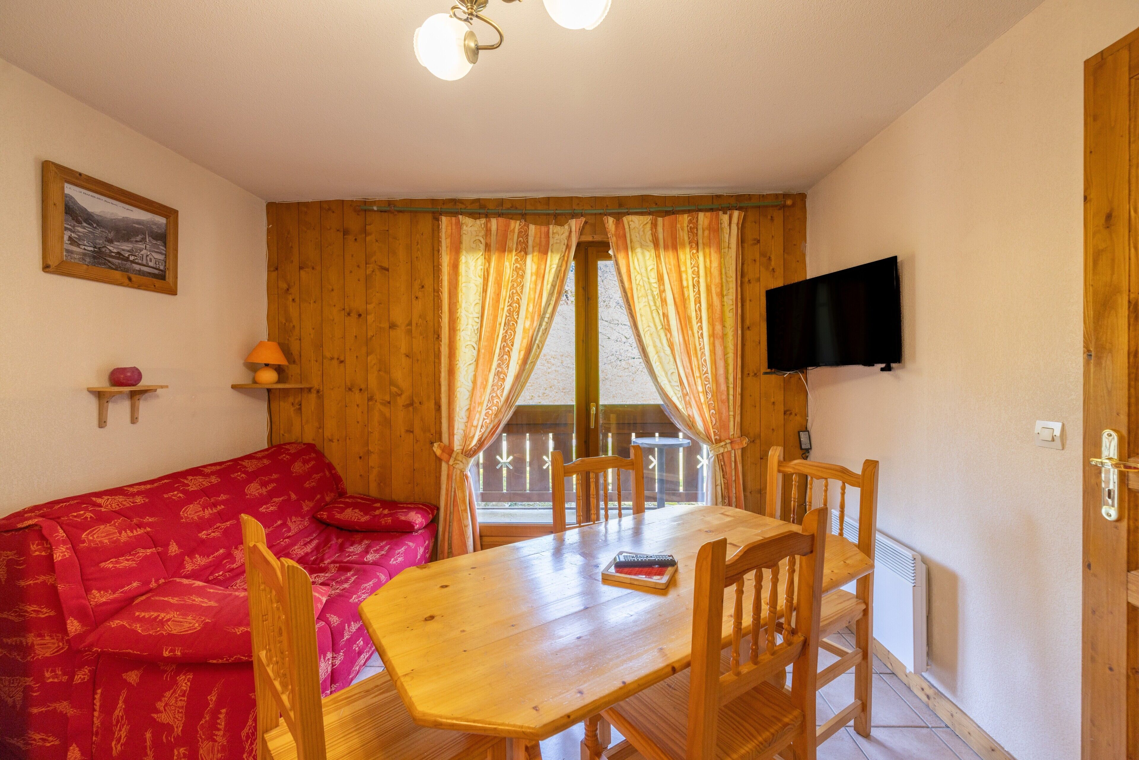 A wooden interior with a sofa, table, chairs, a TV, and a window with curtains.