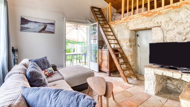 A cozy living room with a sofa, TV, stone wall, wooden staircase, and a door leading outside. - Cottage 'Maison De Campagne' with Private Terrace, Private Garden and Wi-Fi (GIGNAC)