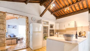 A kitchen with white cabinets, a refrigerator, a dining area with a sofa and table, and a stone wall. - Cottage 'Maison De Campagne' with Private Terrace, Private Garden and Wi-Fi (GIGNAC)