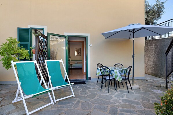 A stone-floored patio with outdoor furniture, a table with a tablecloth, and a large umbrella.