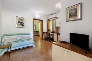 Ein Zimmer mit einem Bett, einem Fernseher, einem Esstisch, Stühlen und einem Bild an der Wand.