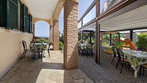 Un patio al aire libre con piso de piedra, mesas con sillas y una estructura de juegos para niños.