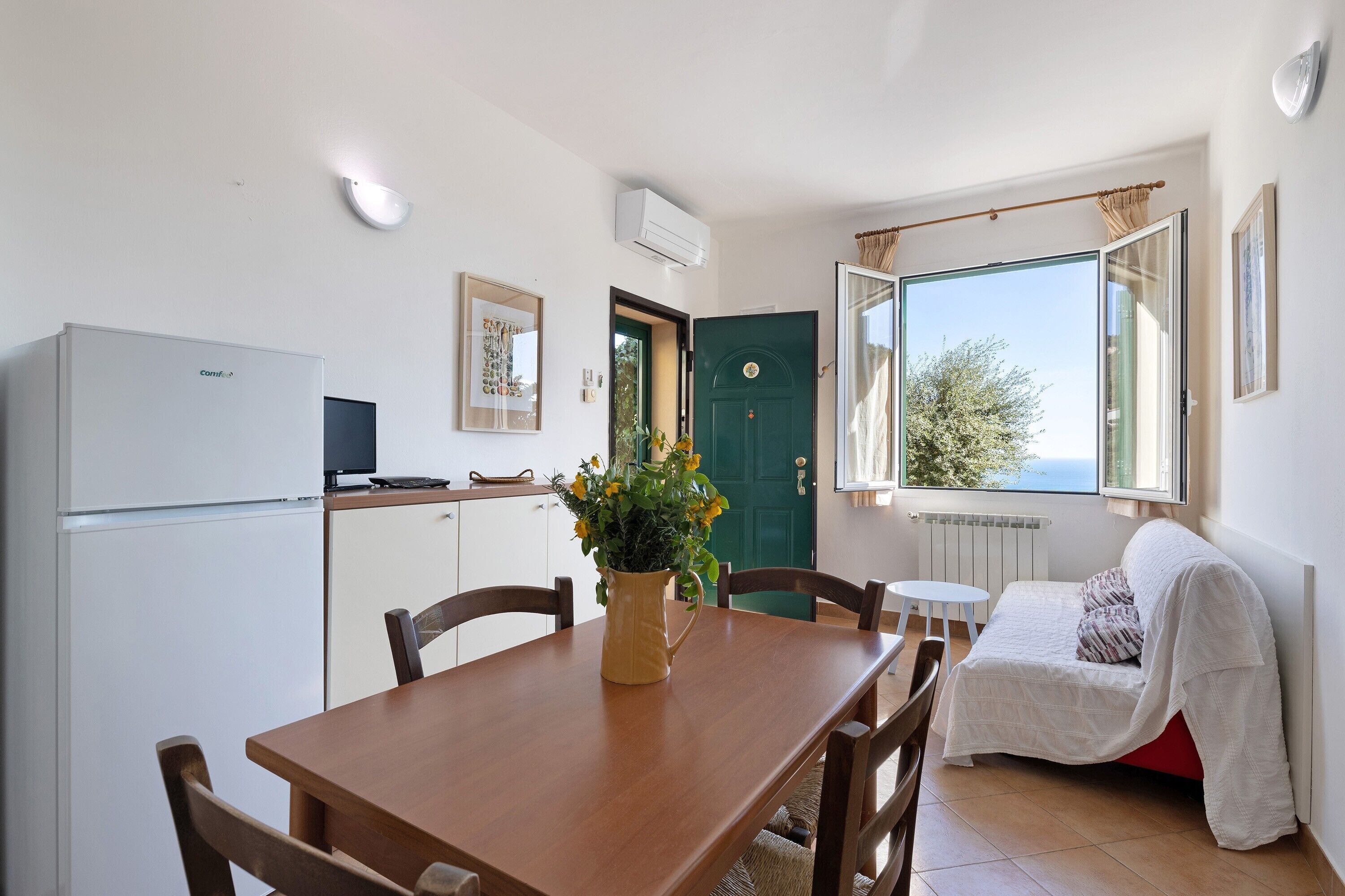 Un espace de vie compact comprenant une table à manger, des chaises, un canapé, une porte verte et une fenêtre donnant sur un beau paysage.