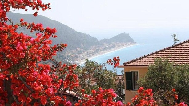 A coastal view with a building featuring a tiled roof, surrounded by red flowering bushes. - Apartment 'La Realidad 3' with Shared Pool, Wi-Fi and Air Conditioning (Finale Ligure)