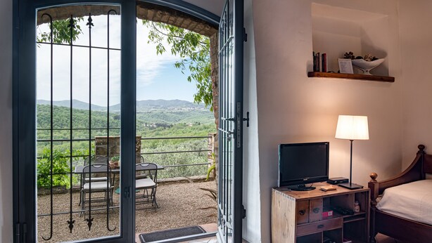 Una habitación con cama, televisión, lámpara, estante con libros y balcón con mesa y sillas.