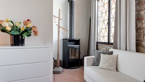 A living room with a white sofa, a fireplace, a window with a view, and a vase of flowers on a shelf. - Apartment 'Fienile' with Private Terrace, Wi-Fi and Air Conditioning (Pelago)