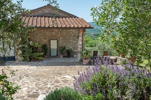 A stone building with a tiled roof, a stone-paved courtyard, and surrounding greenery. - Apartment 'Fienile' with Private Terrace, Wi-Fi and Air Conditioning (Pelago)
