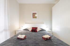 A neatly made bed with a quilted cover, two pillows, a bedside lamp, and a small framed picture on the wall.