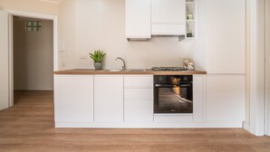 A modern kitchen with white cabinetry, a wooden countertop, a built-in oven, and a small plant. - Holiday Home 'Sa Mariposa' with Balcony, Wi-Fi and Air Conditioning (Cagliari)