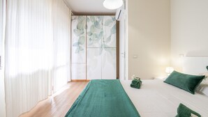 A hotel room with a bed, a green towel, a nightstand, and a window with curtains. - Holiday Home 'Sa Mariposa' with Balcony, Wi-Fi and Air Conditioning (Cagliari)