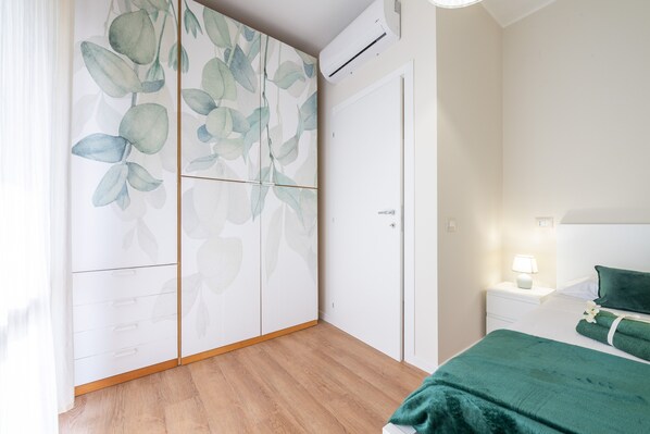 Un dormitorio con una cama, una mesita de noche, una lámpara, una manta verde y un armario con estampado de hojas.