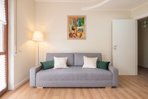 A grey sofa with two pillows, a floor lamp, and a painting on the wall. - Holiday Home 'Sa Mariposa' with Balcony, Wi-Fi and Air Conditioning (Cagliari)