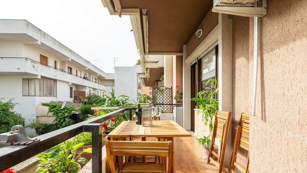 A balcony with a wooden table and chairs, potted plants, and a view of neighboring buildings. - Holiday Home 'Sa Mariposa' with Balcony, Wi-Fi and Air Conditioning (Cagliari)