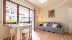 A living room with a sofa, a dining table with chairs, a lamp, and a painting on the wall. - Holiday Home 'Sa Mariposa' with Balcony, Wi-Fi and Air Conditioning (Cagliari)