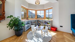 Una habitación con ventanal, planta en maceta, mesa con sillas y estanterías.