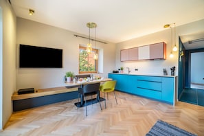 A modern kitchen with a dining area, blue cabinets, a flat-screen TV, and a herringbone wood floor.