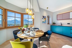 Een eethoek met een houten tafel, stoelen en uitzicht op bergen door grote ramen.