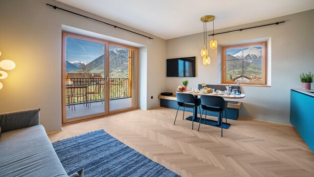 A modern living space with a sofa, dining area, kitchen, and large windows offering mountain views. - Apartment 'Villa Rosa Unterschöberlehof - Anna' with Mountain View, Wi-Fi and Air Conditioning (Meran)