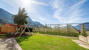 A garden with a wooden swing set, a paved walkway, and a view of mountains. - Apartment 'Villa Rosa Unterschöberlehof - Anna' with Mountain View, Wi-Fi and Air Conditioning (Meran)