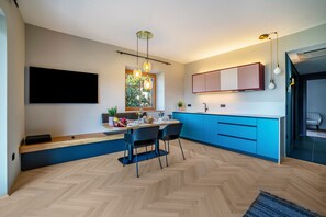 Une cuisine moderne dotée d’une grande fenêtre, de meubles bleus et d’un coin repas avec deux chaises.