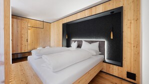 Une chambre moderne avec un plancher en bois, un grand lit avec une literie blanche et une tête de lit sombre.