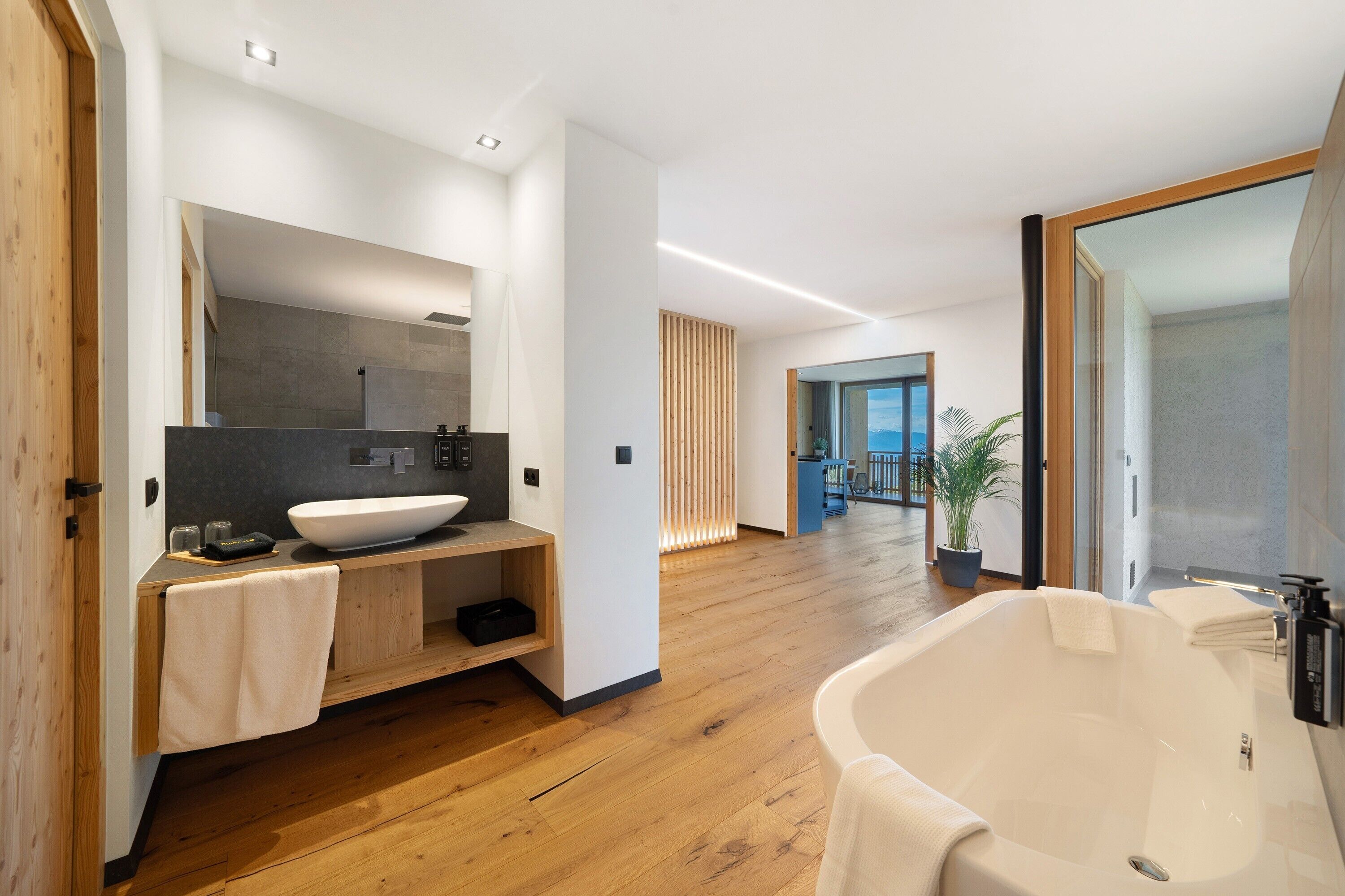 A modern bathroom with a large bathtub, wooden flooring, a large mirror, and a built-in sink.