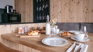 Une table de petit-déjeuner avec une table en bois, des assiettes, une machine à café et un porte-bouteilles fixé au mur.