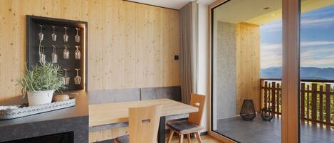 Un espace repas moderne avec un mur en bois, une porte-fenêtre coulissante donnant sur un balcon et une plante en pot.