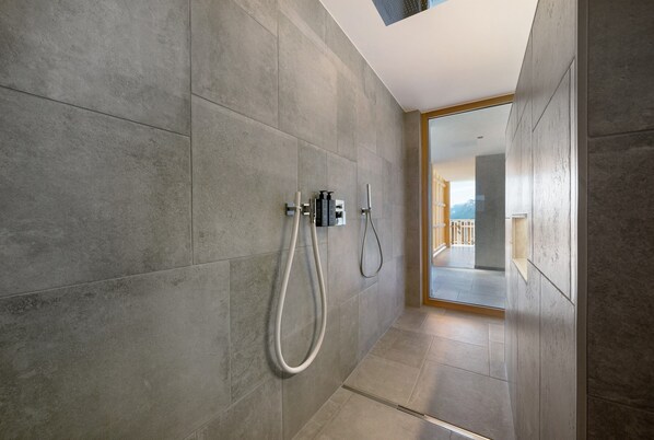 A modern bathroom with grey tiles, a shower with a handheld hose, and a glass door leading to a balcony. - Apartment ‘Lodge Rosmarin’ with mountain views, private terrace, private sauna and whirlpool (Mölten)