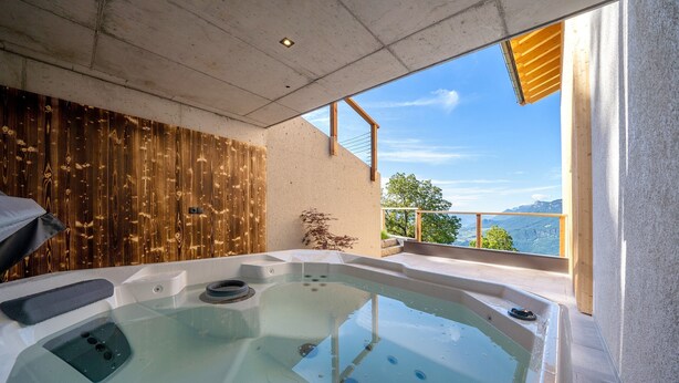 A hot tub with a wooden wall backdrop and a view of mountains.