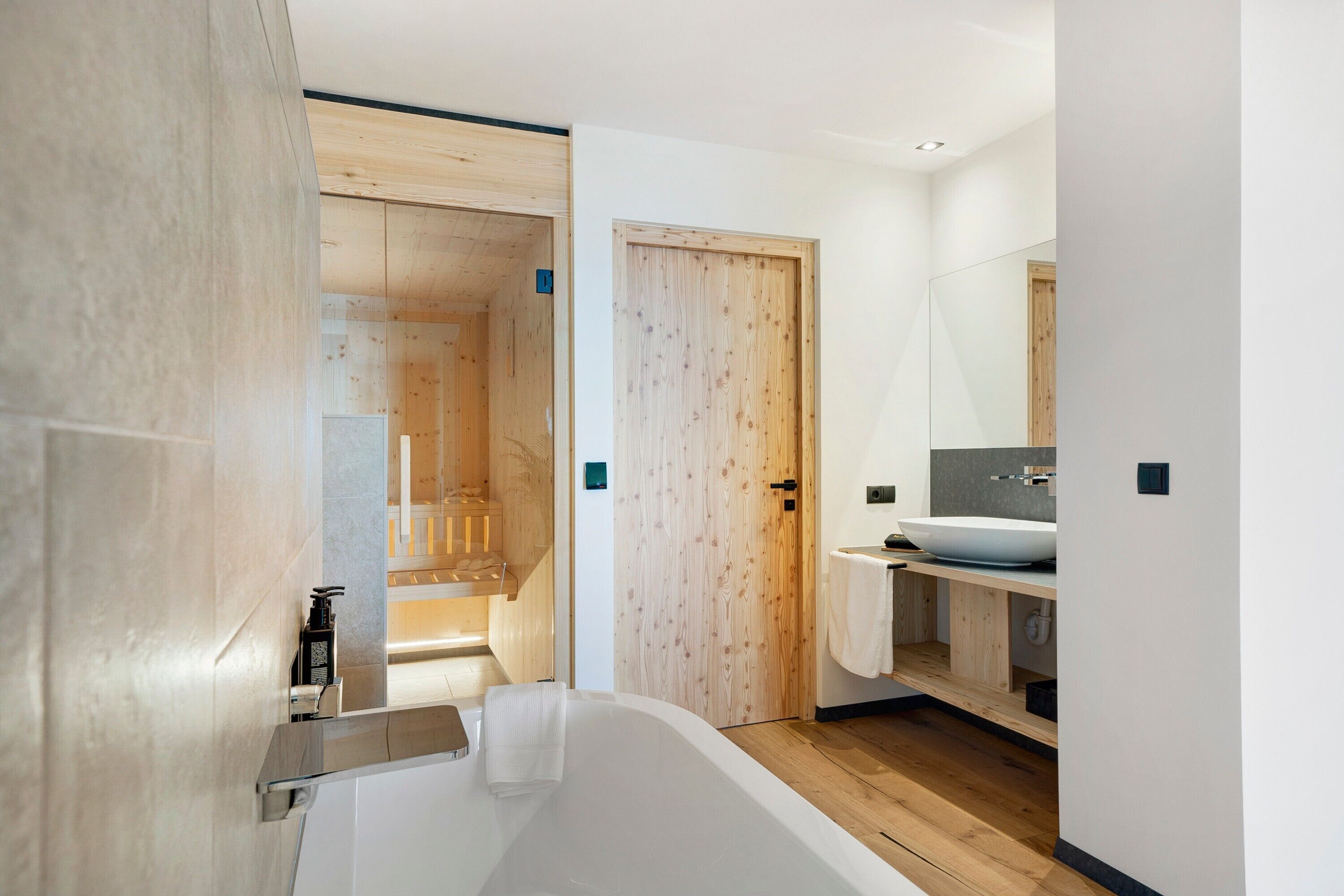 Ein modernes Badezimmer mit einer Badewanne, einer Holztür und einem großen Spiegel.