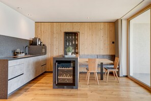 A modern kitchen with a built-in wine cooler, wooden paneling, and a dining area with a table and chairs. - ‘Lodge Melisse’ holiday flat with mountain views, private terrace and private sauna (Mölten)