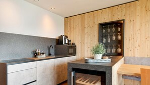 A modern kitchen with a wine refrigerator, built-in appliances, and a wooden accent wall. - ‘Lodge Melisse’ holiday flat with mountain views, private terrace and private sauna (Mölten)