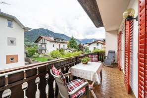 Ein Balkon mit Tisch und Stühlen, Blick auf Häuser und Berge sowie ein rotes Tor.