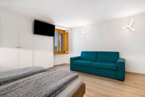 Una habitación moderna con una cama, un sofá color turquesa, un televisor montado en la pared y un ventanal con marcos de madera.
