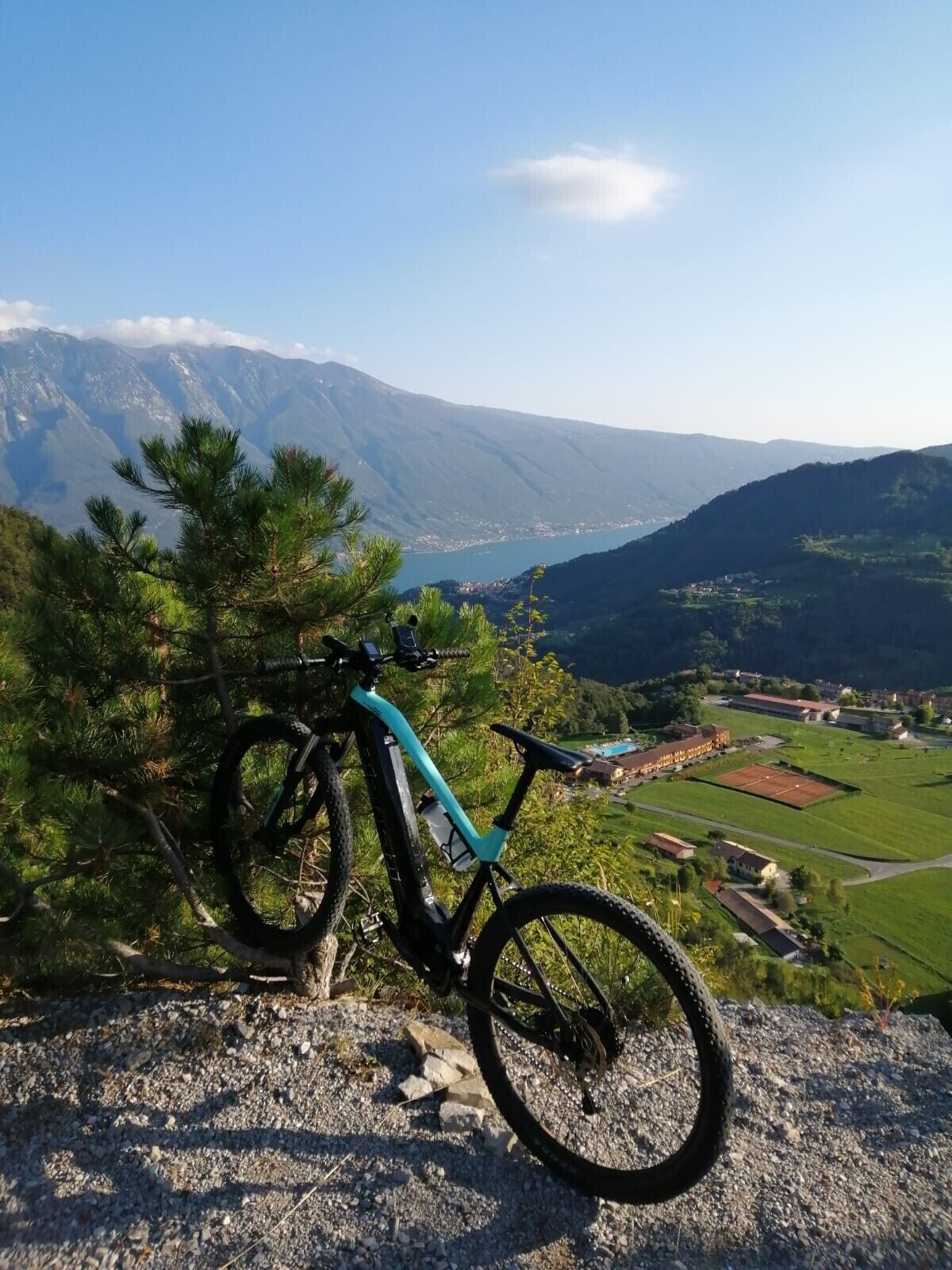 Un vélo tout-terrain est garé sur un terrain rocheux, offrant une vue sur une vallée, des montagnes et un lac.
