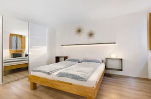 A bedroom with a wooden bed, a mirror, bedside tables, and wall-mounted lights.