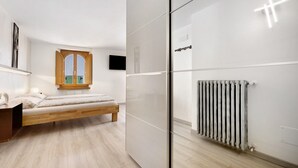 Een moderne slaapkamer met een bed, een houten nachtkastje, een radiator en een raam met uitzicht.