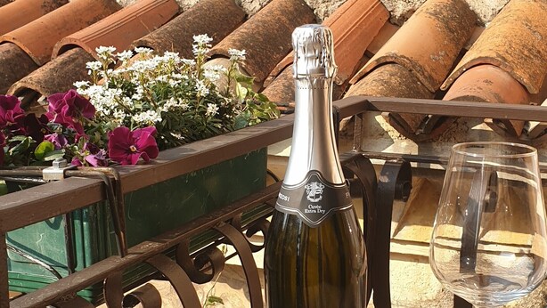 Een terras tafel met een fles Casa Cava wijn, een glas en een bloemstuk.