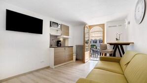 Een moderne woonruimte met een flatscreen televisie, een kitchenette, een bank en een eethoek.