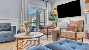 Ein Wohnzimmer mit einer Couch, Sesseln, einem Couchtisch und einem an der Wand montierten Fernseher.