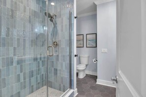 Een badkamer met een glazen douchecabine, een toilet en twee afbeeldingen in lijsten aan de muur.