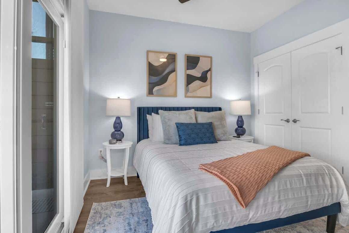Une chambre à coucher avec un lit, deux lampes fixées au mur, une armoire blanche et des œuvres d’art abstraites accrochées au mur.