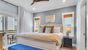 Ein Schlafzimmer mit einem Bett, Nachttischen, einer Bank, einem Deckenventilator und einem Fenster mit Jalousien.