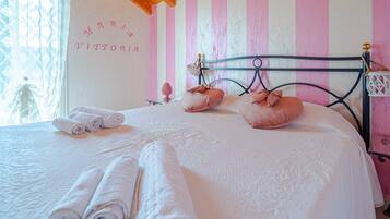Un letto rifatto con cura, asciugamani arrotolati, una testiera decorativa e una parete con un nome.