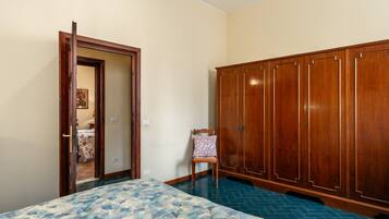 A bedroom with a bed, a wooden wardrobe, a chair, and a door leading to another room.