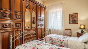 A bedroom with two beds, a wooden wardrobe, a mirror, a nightstand with a lamp, and a floral painting on the wall. - Holiday Home 'Bellavista Altopascio' with Private Terrace and Wi-Fi (Altopascio)