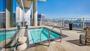 A rooftop pool with clear glass walls, a view of the cityscape, and a bench.