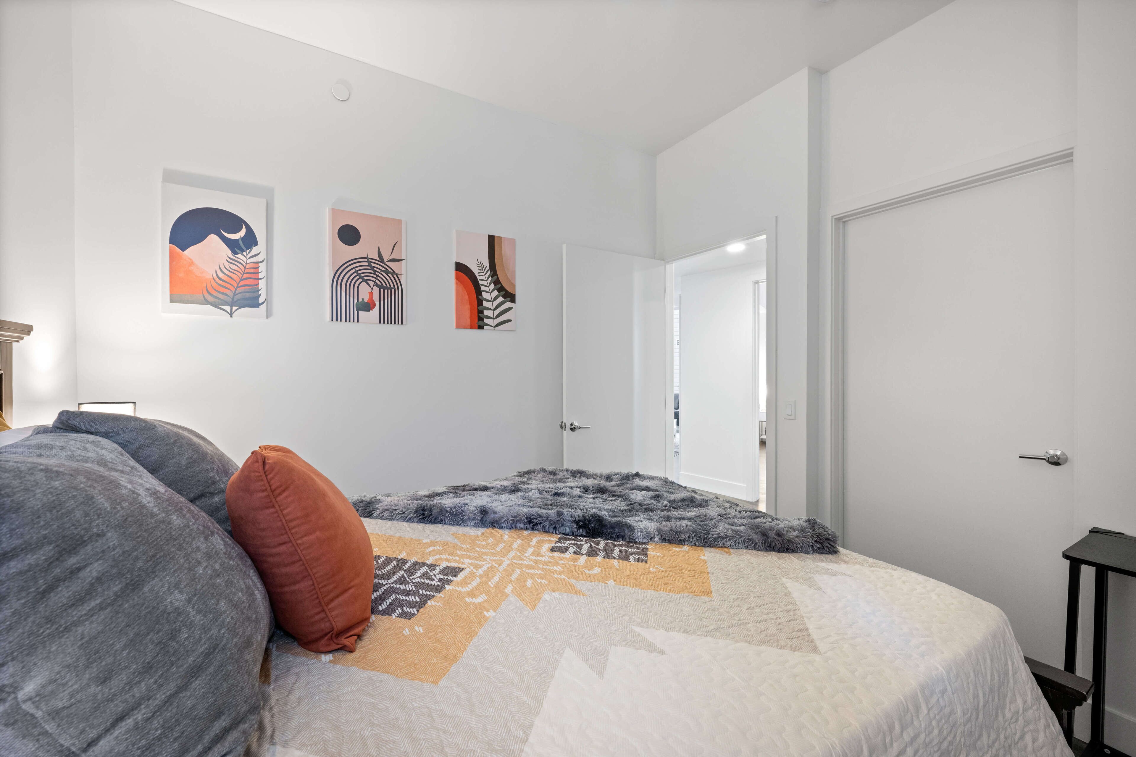 Quarto com cama, almofadas, colcha e três quadros na parede.